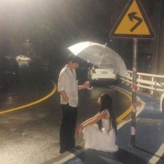 a man holding an umbrella next to a woman on the side of a road at night