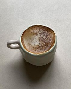 a cappuccino sitting in a white cup on a gray surface with its saucer