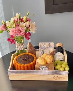 a wooden tray with some food and wine in it on a table next to a vase