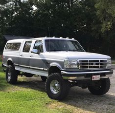 a large white truck parked on top of a grass covered field in front of trees