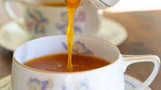 a cup filled with liquid being poured into the mugs and saucers on top of each other