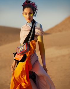 a woman in an orange and pink dress is walking through the desert with her hand on her hip