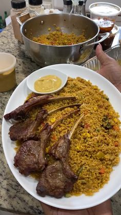 a person holding a plate full of food with meat and rice on the table next to other dishes