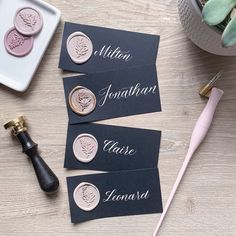 three black and gold place cards with personalized names on them next to a bottle of wine