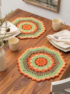 two crocheted placemats sitting on top of a wooden table next to cups