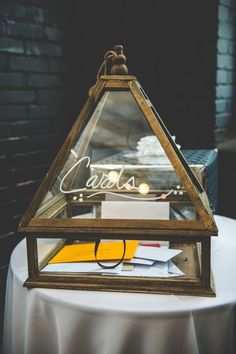 a glass and wood lantern on top of a white table cloth covered round tablecloth