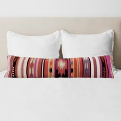 a white bed topped with two pillows and a pillow case covered in colorful striped fabric