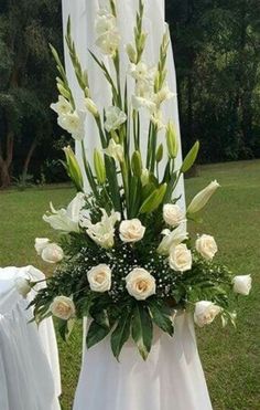 white flowers and greenery are arranged on the back of an outdoor ceremony chair at a park