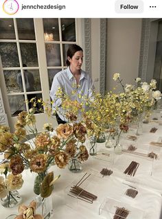 a woman standing in front of a table filled with vases full of yellow and white flowers