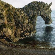 a horse standing on top of a beach next to the ocean in front of a rock formation