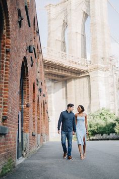 an engaged couple walking in front of the brooklyn bridge