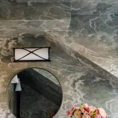 a bathroom with a round mirror on the wall next to a vase filled with flowers