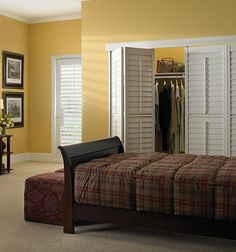 a bedroom with yellow walls and white shutters