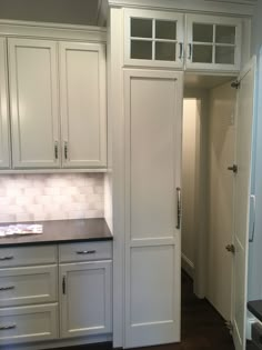 an empty kitchen with white cabinets and black counter tops in front of the pantry door