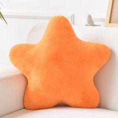 an orange star pillow sitting on top of a white couch next to a potted plant