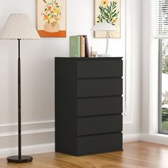 a black chest of drawers in front of a white wall and floor with a lamp on it