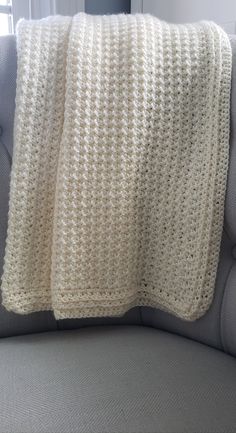 a white crocheted blanket sitting on top of a gray couch next to a window