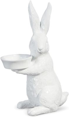 a white ceramic rabbit holding a bowl in its mouth and sitting on it's hind legs