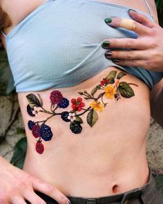 a woman's stomach with berries and leaves on it, while she is wearing a blue top