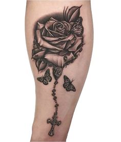 a black rose and cross tattoo on the right leg with two butterflies around it that is attached to a chain