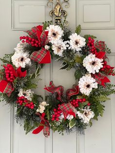 a christmas wreath hanging on the front door with red and white flowers, greenery and berries