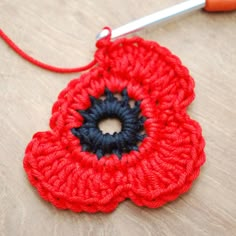 a crocheted red flower with blue center sits on a table next to a pair of scissors