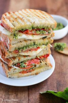 a stack of grilled sandwiches with pesto and tomato on them sitting on a white plate