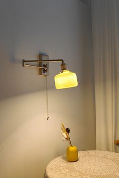 a yellow vase sitting on top of a table next to a wall light and lamp