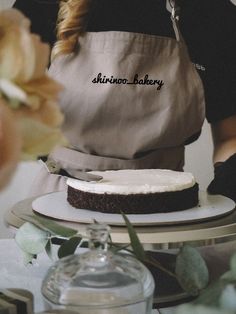 a woman in an apron is decorating a cake with white frosting and flowers