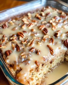 a close up of a cake in a pan on a table with pecans and icing