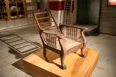 an old chair sitting on top of a wooden platform in front of a book shelf