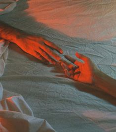 two hands reaching towards each other while laying in bed with white sheets and red light