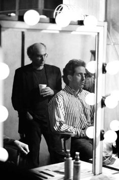 black and white photograph of two men in front of a mirror with lights around them