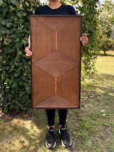 a person standing in front of a bush holding up a large piece of art made out of wood