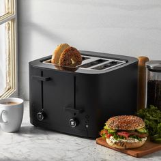 a black toaster with two sandwiches on it next to a cup of coffee and a spoon