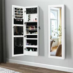 a white mirrored medicine cabinet with jewelry hanging from it's doors and two mirrors on the wall