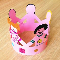 a paper crown with two children on it sitting on top of a wooden table next to each other