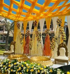 an outdoor wedding setup with yellow and white flowers on the ground, decorated in gold and orange