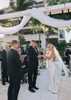 a bride and groom exchanging vows at their wedding in front of an oceanfront hotel