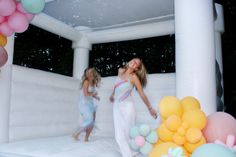 two young women are playing in an inflatable pool with balloons and streamers