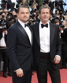 two men in tuxedos standing next to each other at a red carpeted event