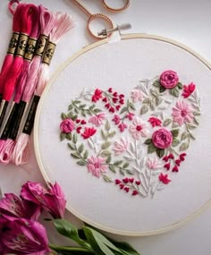 a heart shaped embroidery on a table next to some flowers and two crochet hooks