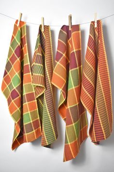 four orange and green plaid towels hanging on a clothes line with pegs to dry them