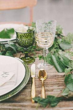 the table is set with green and white plates, silverware, and greenery