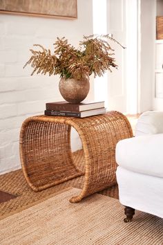 a wicker table with a plant on top and some books in the corner next to it