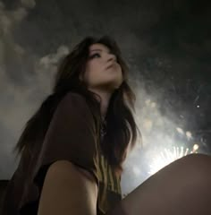 a woman sitting on the ground with fireworks in the sky behind her looking up at something