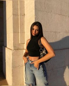 a woman standing in front of a wall with her hand on her hip and looking at the camera