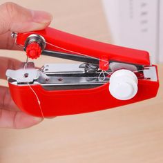 a person is holding a red stapler with white buttons on the handle and one hand