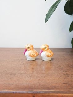 two small figurines sitting on top of a wooden table next to a potted plant