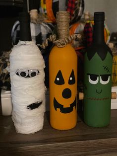 three wine bottles decorated to look like pumpkins and ghost faces with yarn wrapped around them